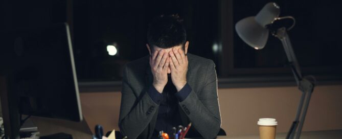 time. A person with their head in their hands whilst sat at a desk